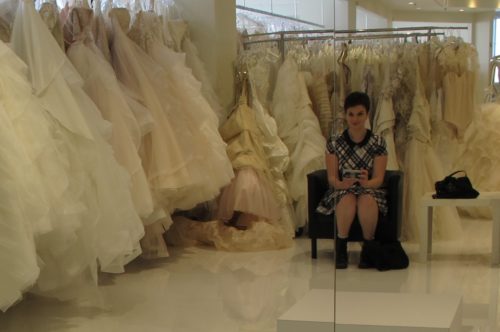 Bride in plaid dress contemplates an array of irvory wedding gowns at Le Marriage bridal shop, Los Angeles. Wedding dress shopping. Photo by Barbara Newhall