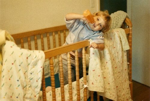 Two-year-old girl enjoys her bottle in her crib with blankies. Photo by BF Newhall