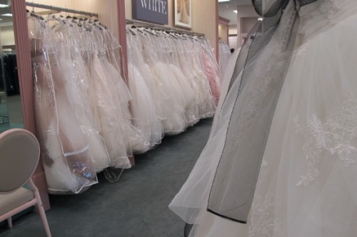 a long rack of fluffy white wedding gowns for sale at David's Bridal Salon, Pinole, CA. Photo by BF Newhall
