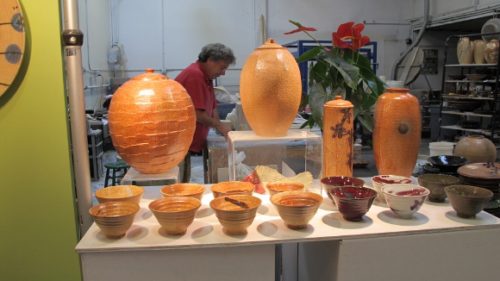 Potter Bob Pool at work in his studio with orange vases and bowls in the foreground. Photo by BF Newhall