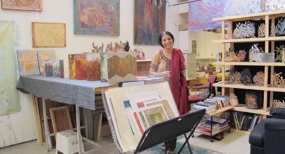 Painter Salma Arastu surrounded by paintings in her Berkeley CA studio. She wears a beige and red sari. Photo by BF Newhall