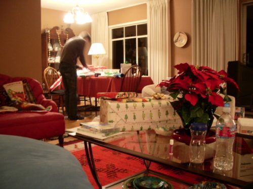 A man wraps his Christmas gifts in a living room cluttered ith decorations and gifts. Photo by BF Newhall