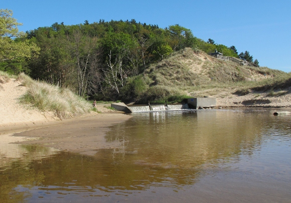 a tree covered dune along lake michigan with a channel and its dam at its base. Photo by BF Newhall
