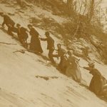 Turn of the 2oth century men and women on vacation struggling to climb the steep sandy slope of Eagle Top on Lake Michigan.