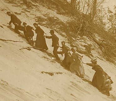 Turn of the 2oth century men and women on vacation struggling to climb the steep sandy slope of Eagle Top on Lake Michigan. 