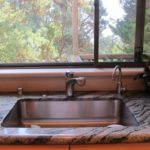 A large stainless steel kitchen sink with a woodsy view out the window. Photo by BF Newhall