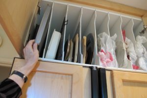 A woman's hand reaches for a cookie sheet in a high cupboard with vertical slats. Photo by BF Newhall
