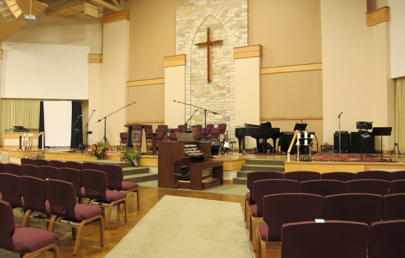 The worship space of the First Evangelical Free Church of Austin with upholstered chairs in row, a simple cross at the front of the room and audio equipment set up for praise worship. Photo by bf newhall