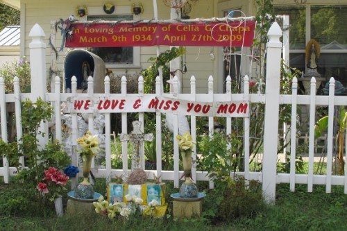 A memorial to Mom on a white picket fence in Austin includes plastic flowers and photos of a woman who died in 2009. Photo by BF Newhall