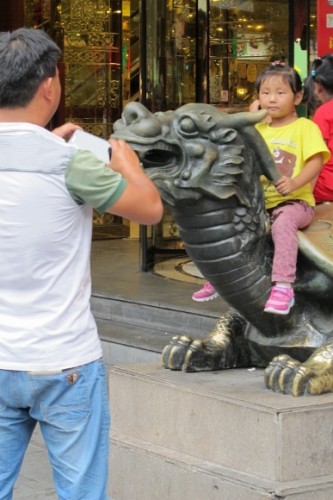 A man takes a photo of a small child sitting on a sculpture dragon in Shanghai's Yuyuan Bazaar. Photo by BF Newhall