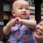 a pudgy faced chinese baby boy is held aloft by a woman who seems to be his grandmother in Shanghai. Photo by bf newhall