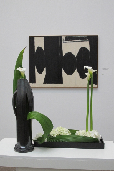 An austere floral design of calas and leaves reflects Robert Motherwell's painting, "At five in the Afternoon, 1950," at the Bouquets to Art show at the de Young. Photo by BF Newhall