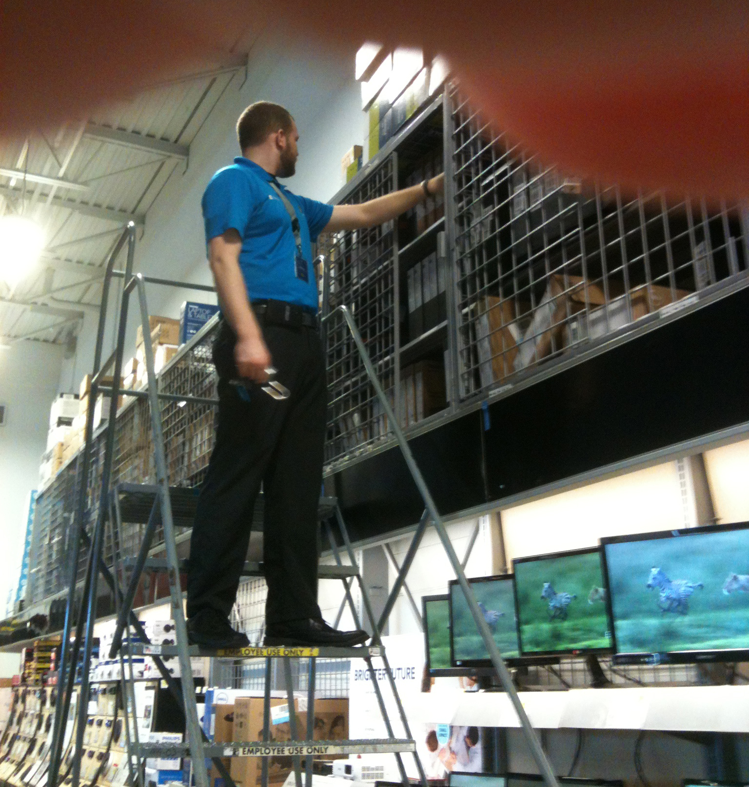 Sales clerk at Best Buy store climbs ladder to pull down a new Toshiba laptop for a customer. Photo by BF Newhall