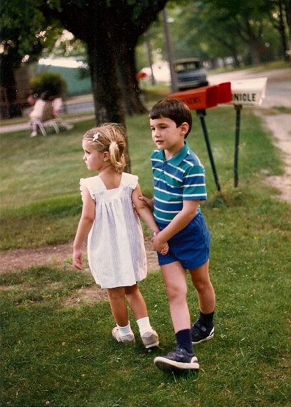 A 5-year-old boy wearing shorts holds on to the arm of a 3-year-old girl in a dress. Photo by BF Newhall