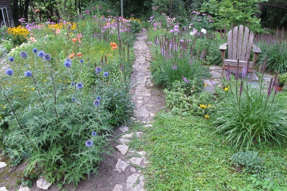 A weathered Adirondack chair sits in the midst of a profusely flowering garden with Liatris and day lilies. Photo by Barbara Newhall w