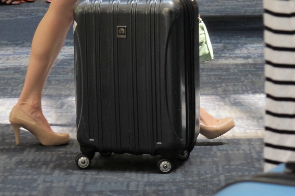 A bare-legged woman wears tan pumps and pull a black carry-on at SFO. Photo by Barbara Newhall