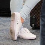A woman at SFO wears shiney white tennies with a hole in the sole. Photo by BF Newhall