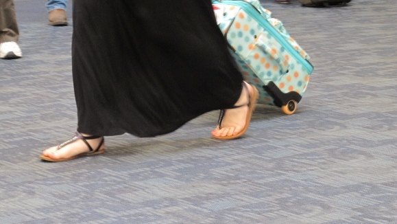 A woman wears long black skirt, sandals pulls a carry-on- at SFO. Photo by Barbara Newhall