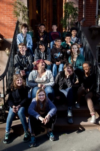 A dozen or so happy teenagers sit on the front steps of a brick building. The editorial board of KidSpirit meets to discuss future issues. Photo c 2014 by Jon Hochman
