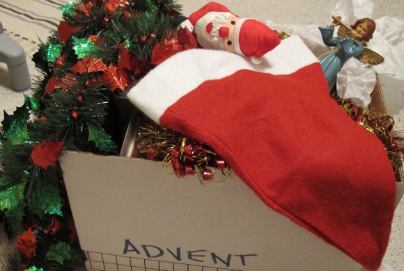 A box marked Advent overflows with Christmas decorations, including an angel, a Santa and shiney tinsel garlands. Photo by Barbara Newhall