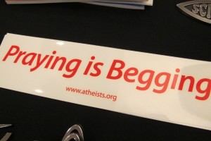 A bumper sticker offered at the Religion Newswriters Conference in 2014 reads "Praying Is Begging." Photo by Barbara Newhall