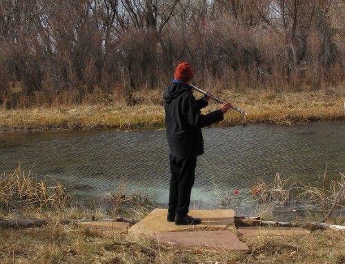 a man plays the flute by a small river in winter. Photo by Barbara Newhall
