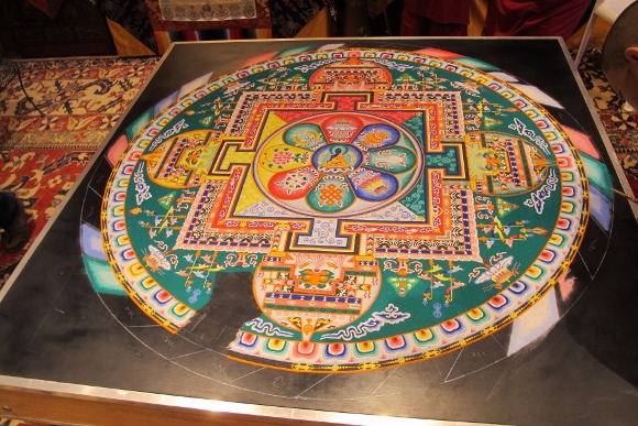A sand painting created by the monks of the Drepung Loseling Monastery of the Geluk school of Tibetan Buddhism that depicts the Immovable Buddha is partly destroyed by accident when a visitor drops her cell phone onto it. Photo by Barbara Newhall