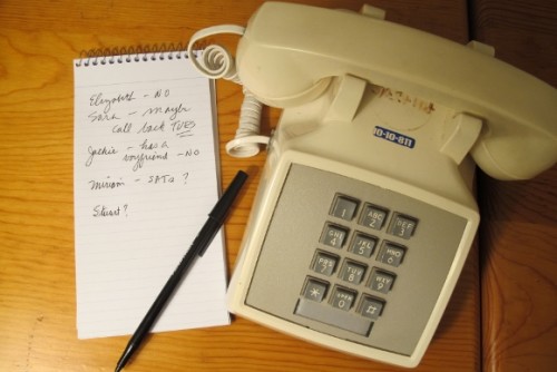 An ivory colored touch-tone telephone, c.irca 1970s, with coiled cord and handset. A babysitter phone list is next to it. Photo by Barbara Newhall