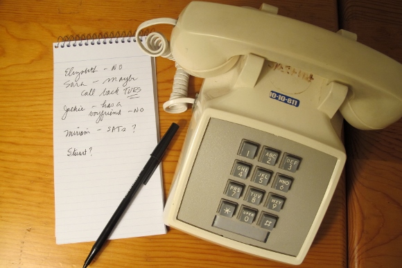 An ivory colored touch-tone telephone, c.irca 1980s, with coiled cord and handset. A babysitter phone list is next to it. Photo by Barbara Newhall