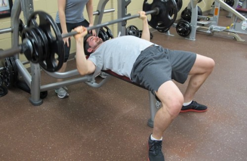 Peter Newhall, a young man in his 30s, bench presses at a gym. Photo by Barbara Newhall
